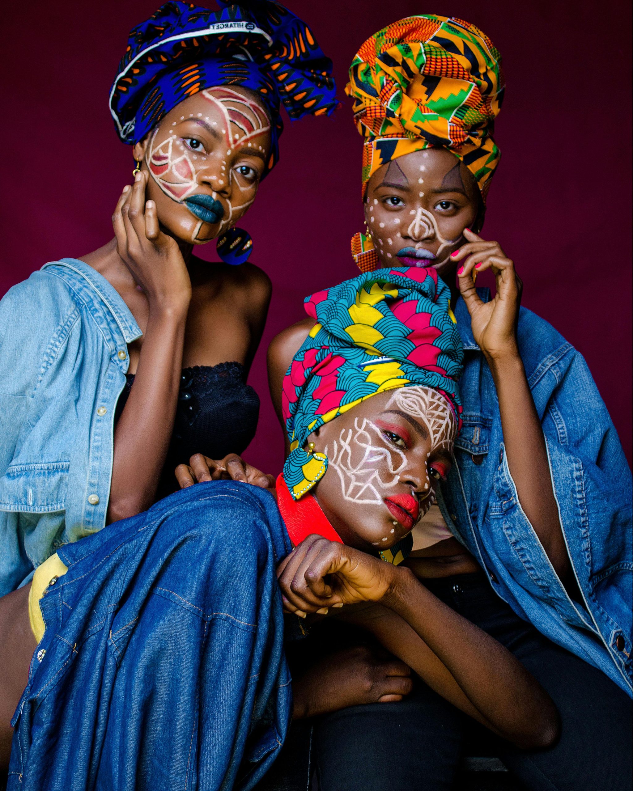 Three women in colorful African outfits with face paint and headdresses celebrating culture.